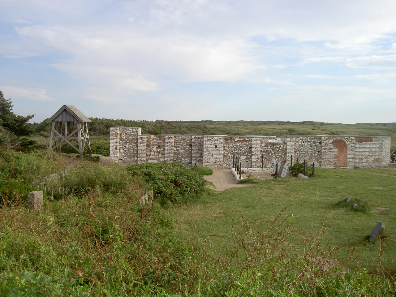 Walls of Mårup Church in Lønstrup, Denmark, after the church was dismantled to prevent its loss into the North Sea. Seen from the north. The graveyard adjacent to the church includes several victims from the British frigate, the Crescent, which sank in December 1808. The Crescent's anchor can be seen behind the wooden bell tower at left.